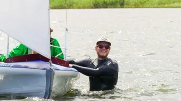 Person pushing small sailboat in water.