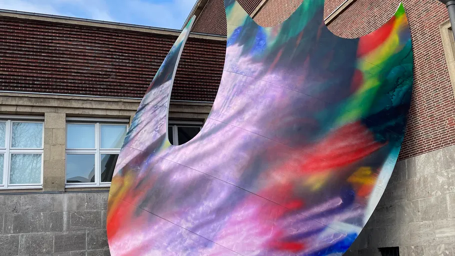 Bunte abstrakte Skulptur vor einem Ziegelgebäude.