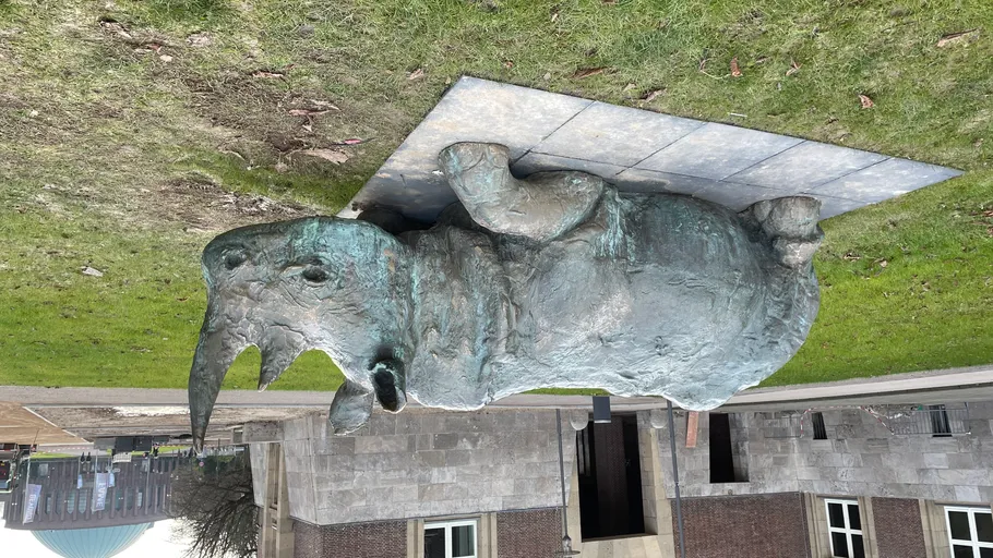 Rhinoceros sculptor on grass near building.