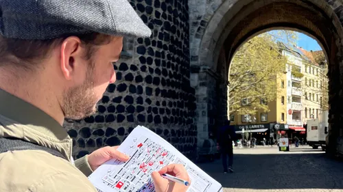 Man studies map near stone archway, city street visible.