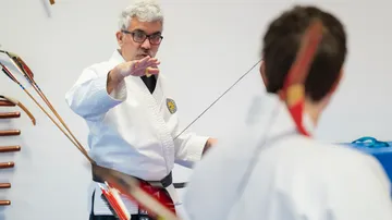 Instructor teaching archery in a dojo setting.