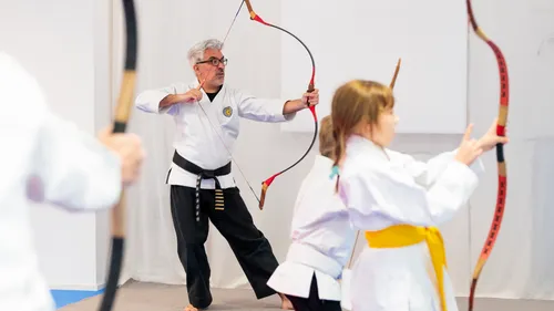 Personen üben Bogenschießen im Kampfsportkurs.