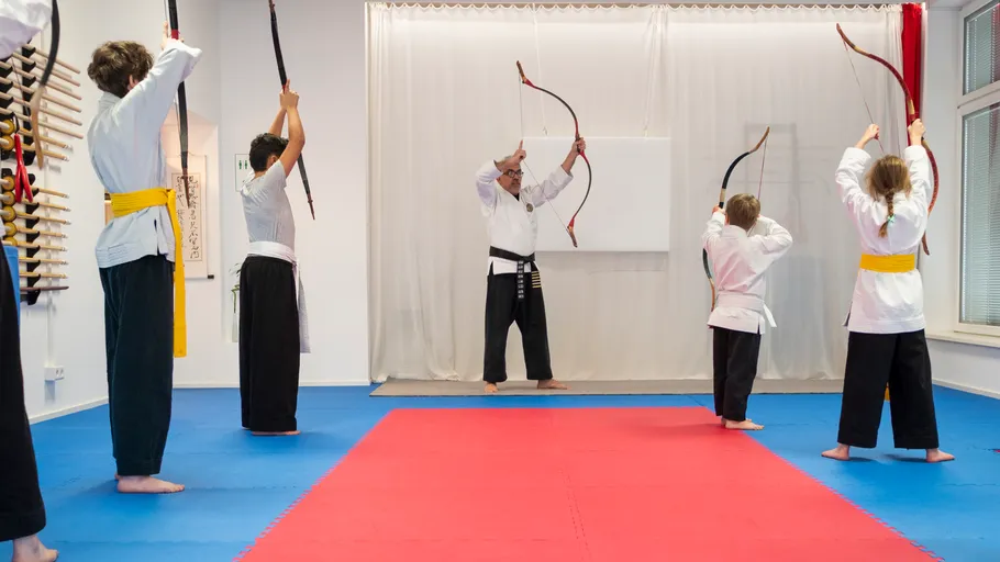 Martial arts class practicing archery indoors.