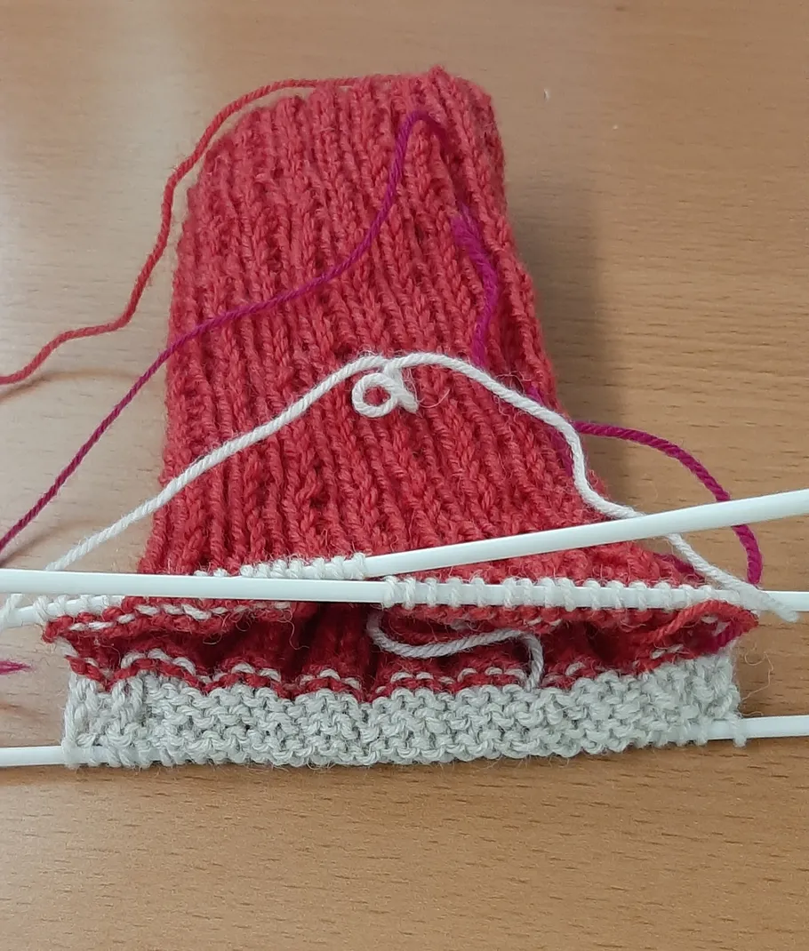Gestrickter Stoff auf Nadeln mit Garn auf Tisch.