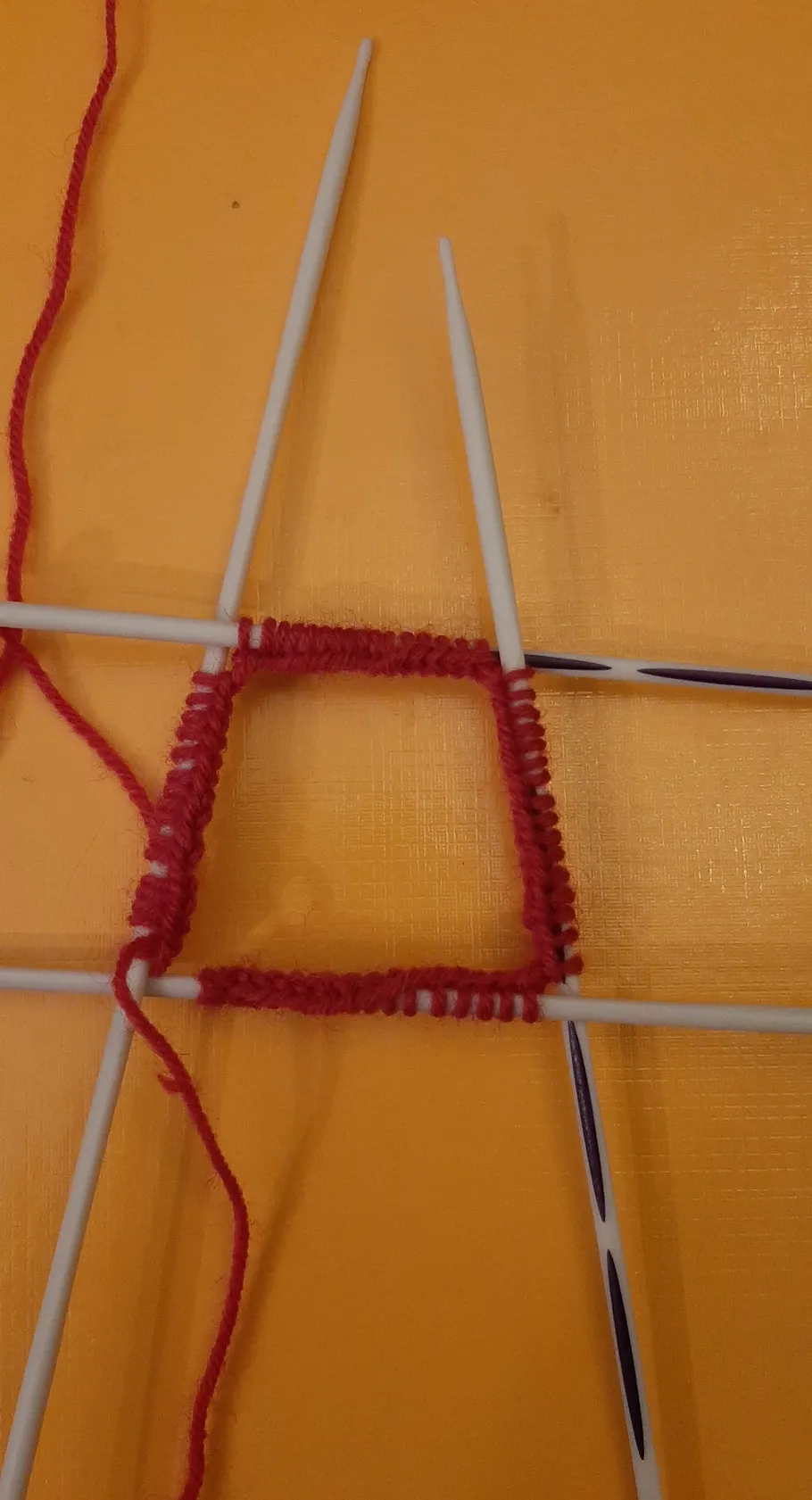 Rotes Garn auf Nadelspiel, orangefarbener Hintergrund.