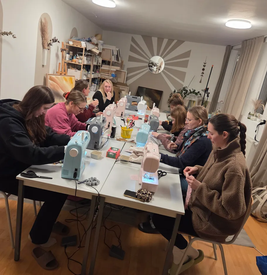 Menschen nähen an Tischen in einem Workshop.