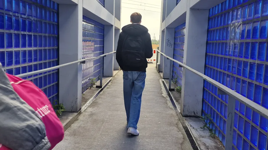 Person walking on blue-glass bridge walkway.