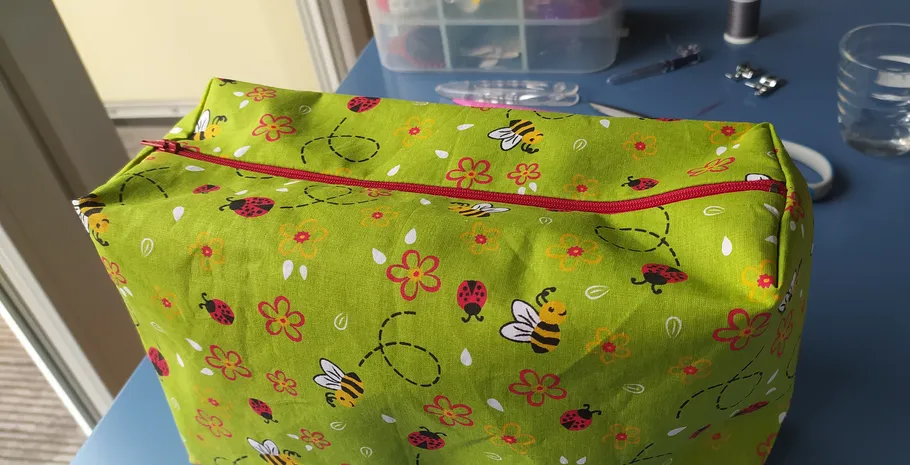 Green fabric bag with bee print on table.