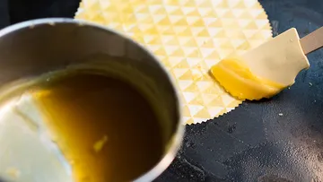 Ein Topf mit flüssiger Substanz, wird auf ein Waffelblatt gestrichen.