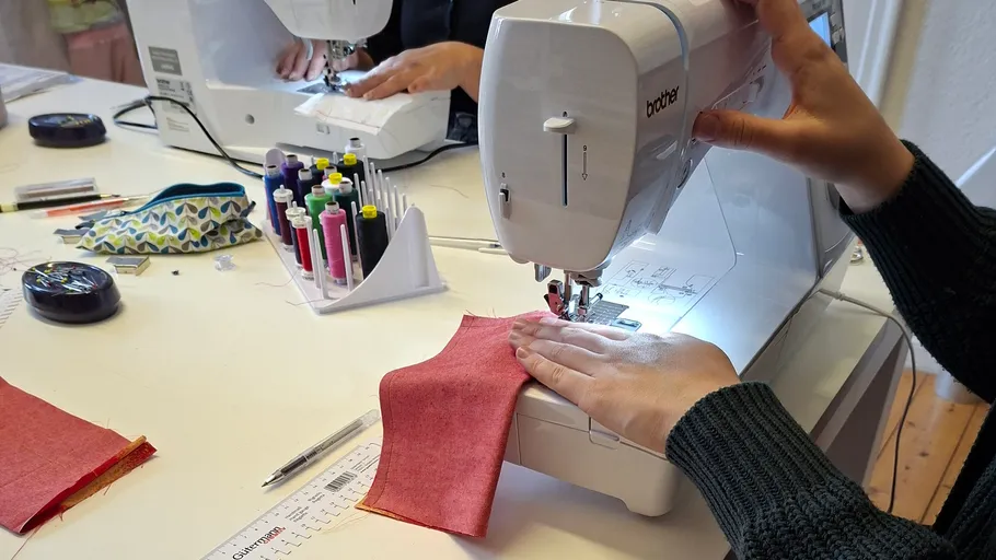 Person sewing red fabric on a machine.