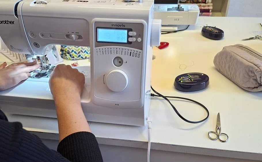 Person nutzt Nähmaschine auf einem Tisch.