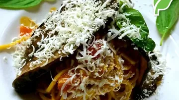 Spaghetti topped with cheese, basil, and eggplant slice.