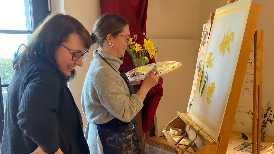 Two women painting flowers in a studio.