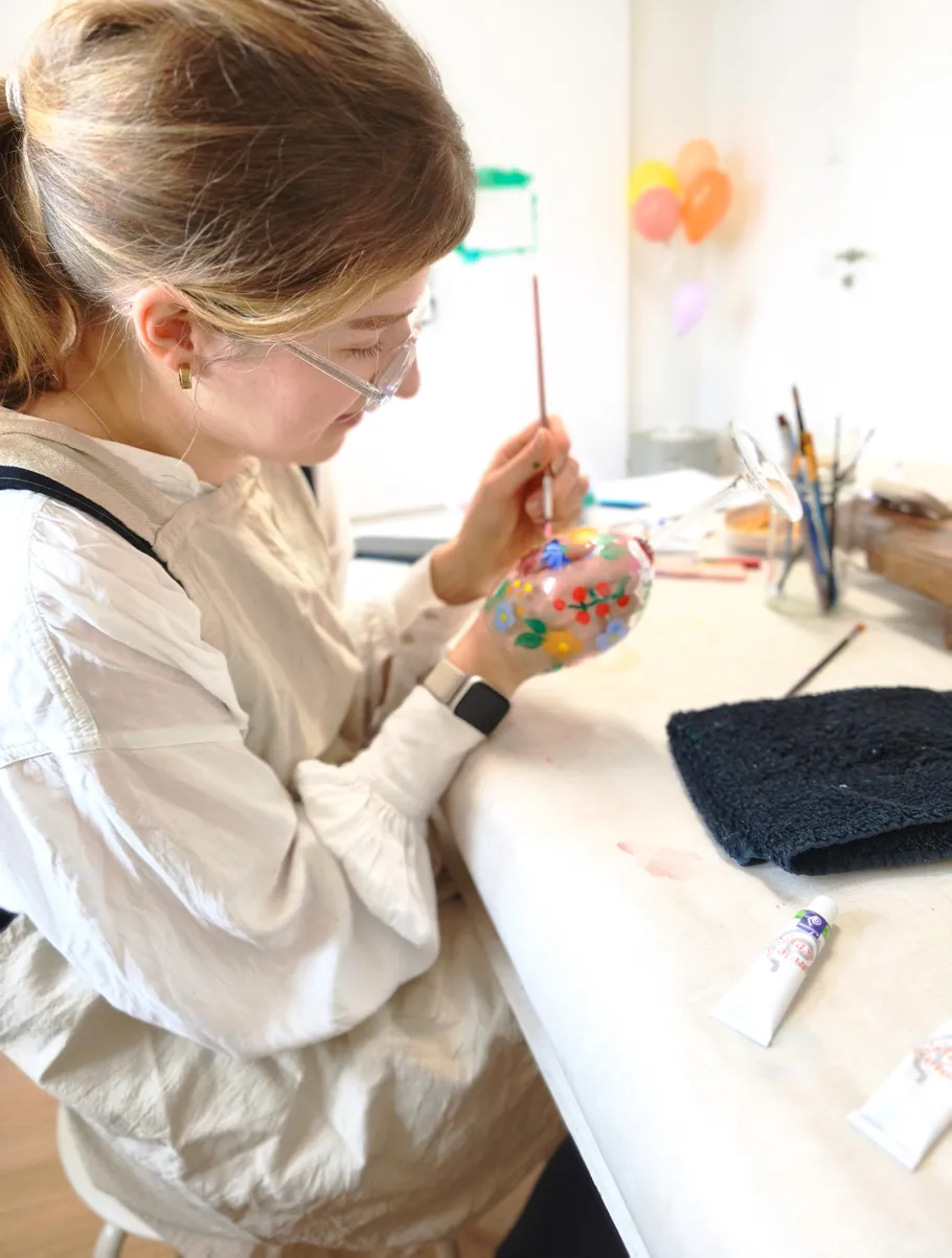 Person painting glass ornament at table.
