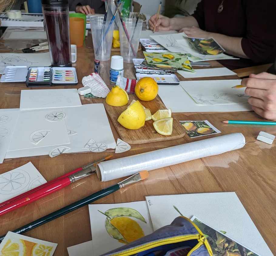 People drawing lemons on table with art supplies.