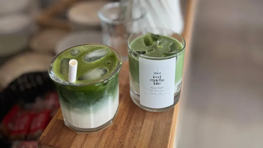 Two iced matcha lattes on wooden counter.