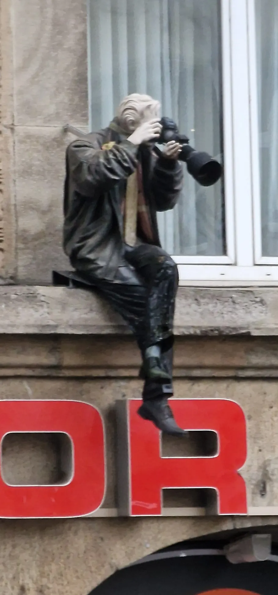 Statue of photographer taking photos, sitting on ledge.