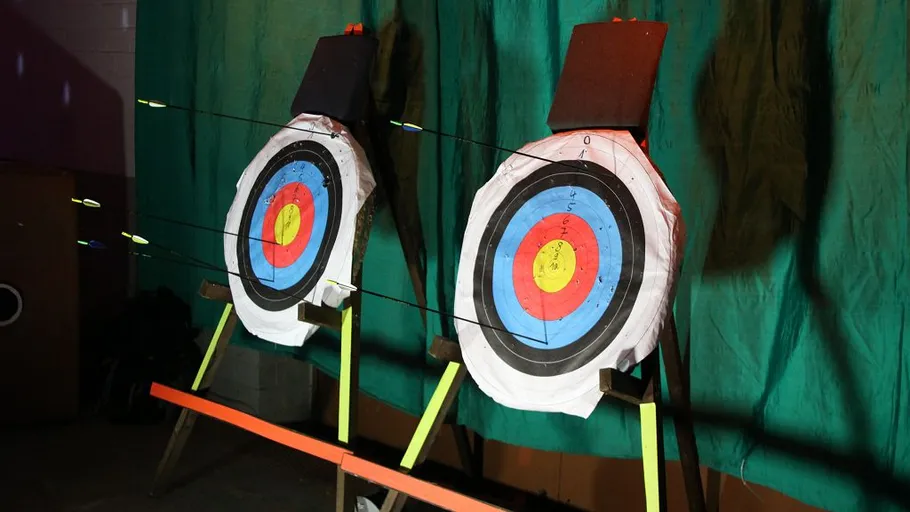 Two archery targets pierced by arrows indoors.