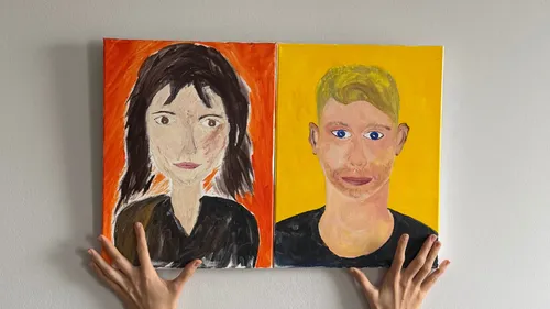 Hands holding two portraits against wall.