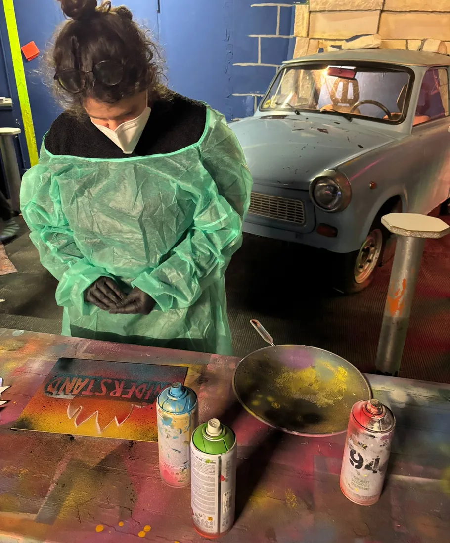 Person sprüht Farbe im Workshop, altes Auto in Nähe.
