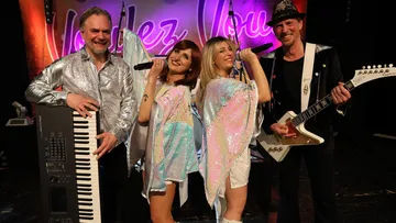 Band mit Instrumenten auf Bühne, bunte Outfits.