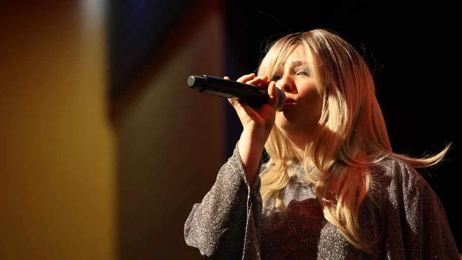 Blonde Sängerin singt auf Bühne mit Mikrofon.