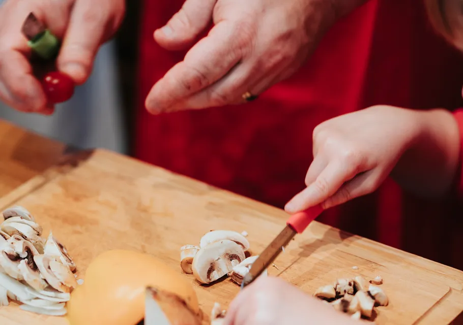 Hands slicing mushrooms on wooden board.