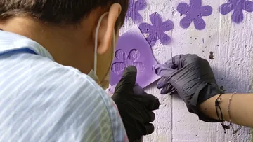 Person spray-paints flowers on a wall.