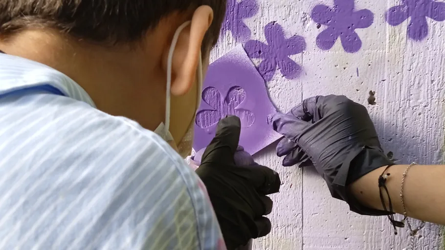 Person sprüht Blumen auf eine Wand.