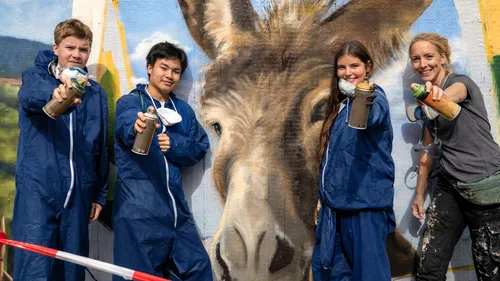 Four people spray painting mural outdoors.
