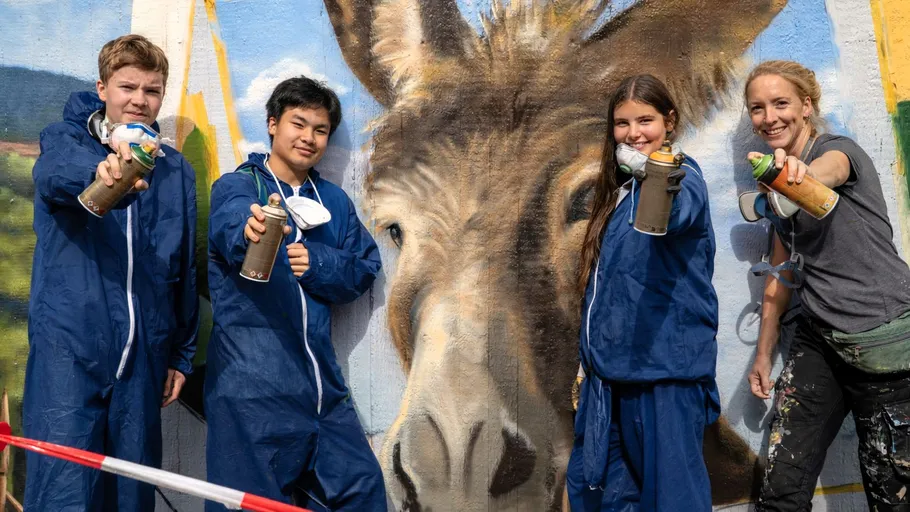 Vier Personen sprühen Wandbild im Freien.