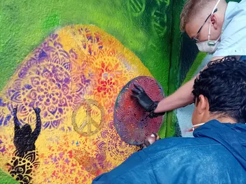 Zwei Personen malen farbenfrohes Wandbild an Wand.
