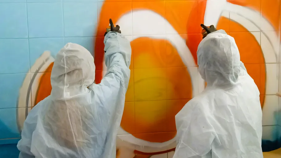 Zwei Personen sprühen buntes Graffiti an Wand.