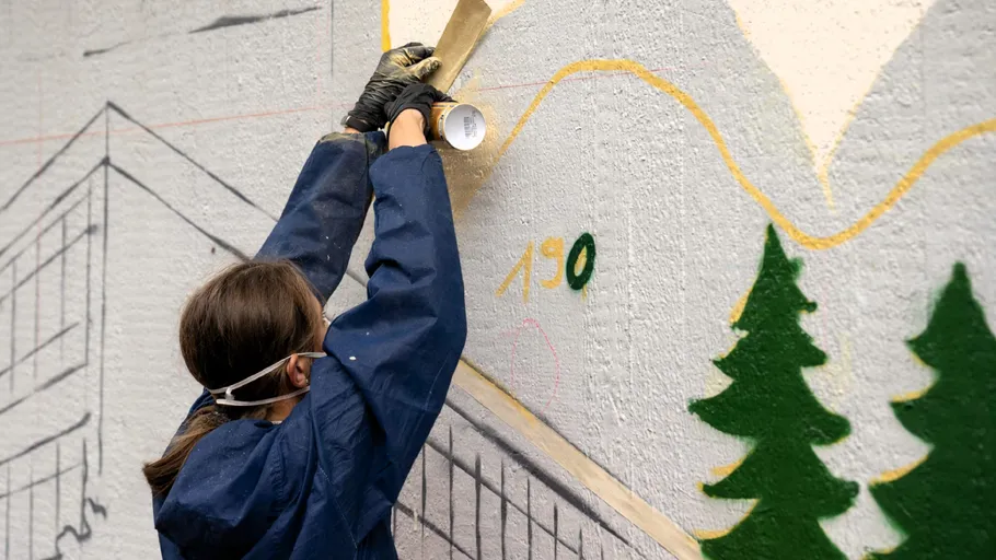 Person malt Wandgemälde an Außenwand.