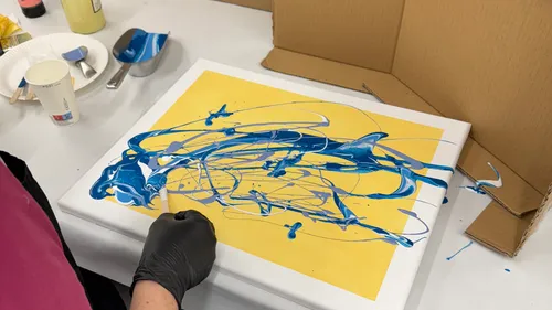 Person creating abstract blue painting on canvas.