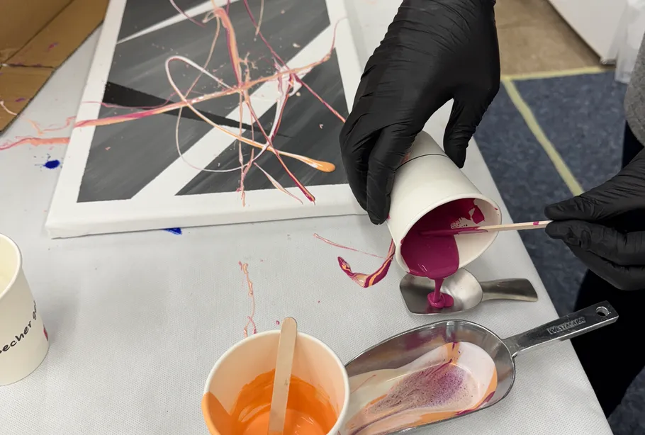 Person pouring paint onto abstract canvas.