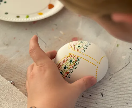 Person painting dotted design on an egg.