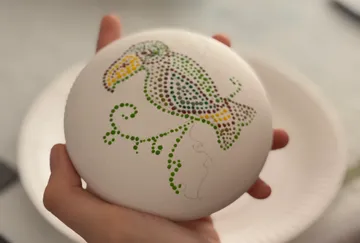 Hand holds painted stone with bird design.