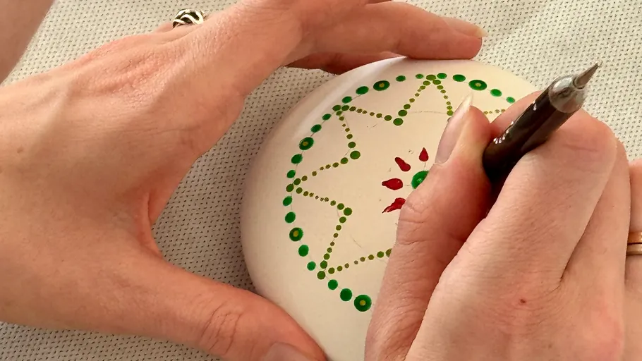 Hands painting mandala pattern on white stone.