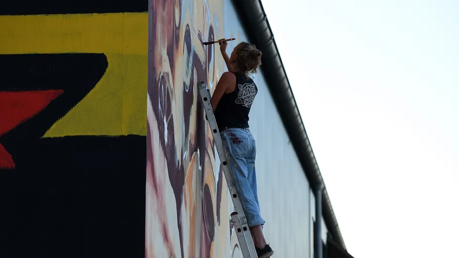 Artist painting on a tall wall using ladder.
