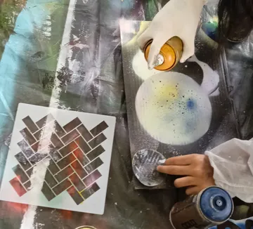 Hands spray painting with stencils on fabric.