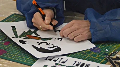 Hands cutting stencil on a table.