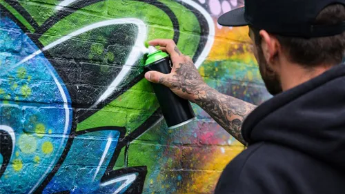 Person sprüht buntes Graffiti auf Wand.