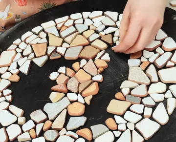 Hand arranging colorful stones in mosaic pattern.