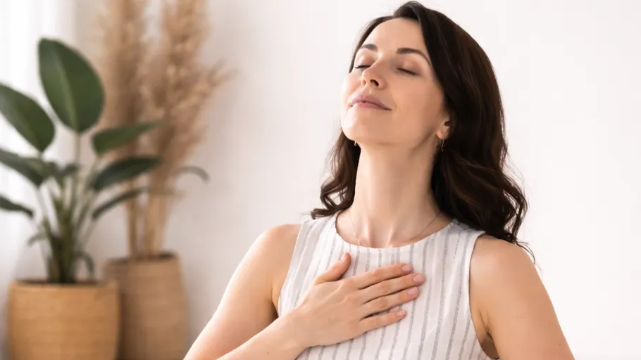 Woman calmly breathing, hand on chest, indoors.