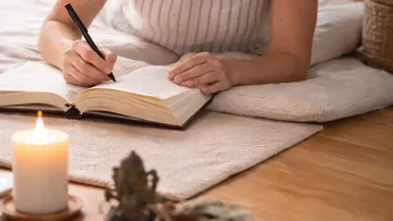 Person schreibt bei Kerzenlicht ins Tagebuch.