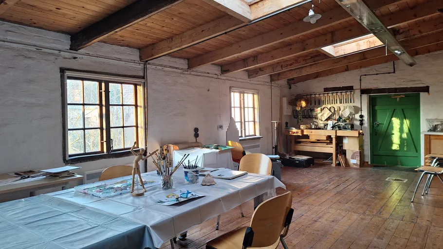 Künstleratelier mit Holzdecke und Tischen.