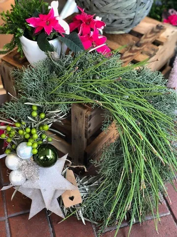 Grüner Kranz mit roten Blumen auf Holzkisten.
