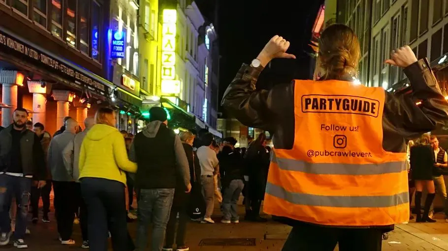 Person wearing 'Partyguide' vest in crowded nightlife street.