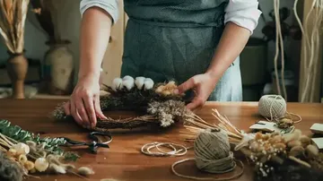 Person making floral wreath on wooden table.